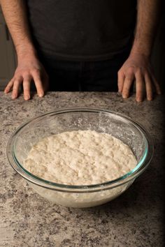 a bowl filled with batter sitting on top of a counter next to a person's hands