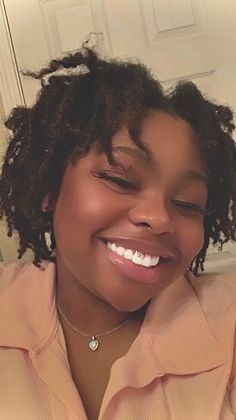 a woman with curly hair is smiling and looking at the camera while wearing a pink shirt