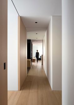 a person walking down a long hallway in a house with white walls and wood floors