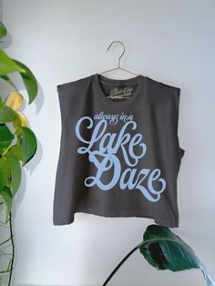 Get all of the summer-y vibes in our oversized retro inspired Lake Daze cropped muscle tank!- Features the phrase "Always in a Lake Daze" in a light blue ink- Screen print transfer that is heat pressed onto each tshirt - Tshirt is a high quality, garment dyed, vintage wash that gets softer after each wash - Oversized fit - Sizing translation: XS/S - M , S/M - L , L/XL - XL , 2XL/3XL - 2XL - 100% Cotton**due to screens & filters color may vary from pictures** Summer Tank Top With Text Print, Blue Graphic Print Muscle Tee, Retro Cropped T-shirt With Text Print For Summer, Blue Casual Muscle Tee With Graphic Print, Summer Sleeveless Tank Top With Text Print, Sleeveless Tank Top With Text Print For Summer, Retro Screen Print Tank Top For Summer, Summer Muscle Tee With Letter Print And Short Sleeves, Summer Streetwear Tank Top With Text Print