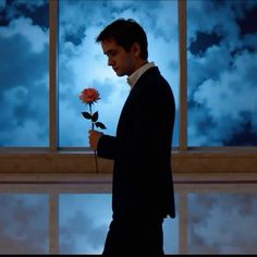 a man in a suit holding a rose up to his face and looking out the window