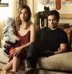 a man and woman sitting on a couch with a baby in their lap looking at the camera