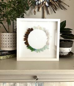 a white frame sitting on top of a dresser next to a potted plant and books