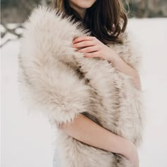 a woman is standing in the snow with her arms crossed and she is wearing a fur coat