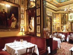 a dining room with paintings on the wall and tables set for two, along with white tablecloths