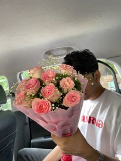 a man sitting in the back seat of a car holding a bouquet of pink roses