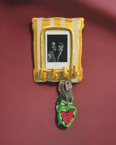 a gold frame hanging on the wall with a keychain attached to it and an image of two people