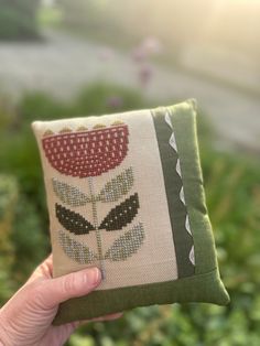 a hand holding up a small pillow with a flower design on it's side