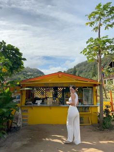 a woman standing in front of a small yellow building with a bar on the side