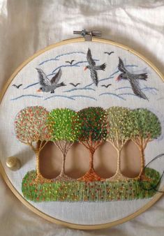 the birds are flying over the trees in the embroidery