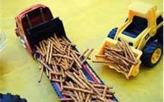 two toy trucks are next to a pile of wood sticks on a yellow tablecloth