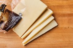 several pieces of cheese sitting on top of a wooden table next to a bag of cheese