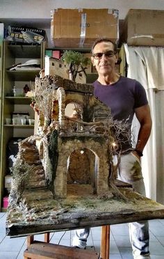 a man standing in front of a fake house made out of wood and mossy materials