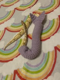 a crocheted banana laying on top of a rainbow colored bed sheet with an odd shaped object in the middle