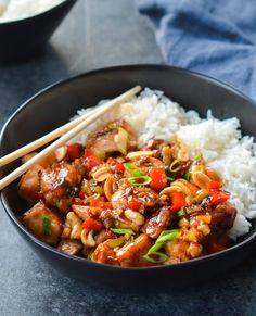 a black bowl filled with rice and stir fried food next to chopsticks on the side