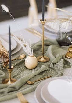 the table is set with white plates and silverware, gold candlesticks and green napkins