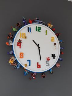 a clock made out of legos with numbers on the face and hands, in front of a gray background