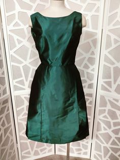 This is a gorgeous unlabelled as to its maker teal green tafetta cocktail dress from the late 50s or early 60s. The dress is sleeveless with a fitted bodice and scooped neckline, is waisted then to a flared skirt section with an extra panel of fabric at the front and wide box pleated at the back. The below knee length skirt section is pelham lined which gives the skirt structure . The back of the dress has a deep V to the  waist and has a large bow centre back giving the dress a bit of a dramati 1950s Style Green Evening Dress, Green 1950s Style Evening Dress, 1950s Style Green Formal Dress, Green 1950s Style Formal Dress, Green Formal Dress In 1950s Style, Early 60s, Scooped Neckline, Large Bow, Box Pleats