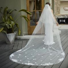 a woman wearing a white veil with flowers on the bottom is walking down a wooden deck