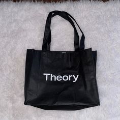 a black tote bag with the word theory printed on it sitting on a white carpet