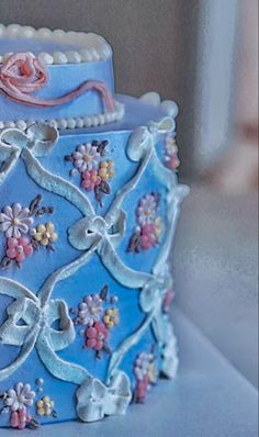 a decorative blue cake with flowers on it's sides and frosting around the edges