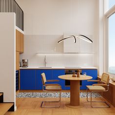 a modern kitchen with blue cabinets and wooden flooring, along with a round dining table surrounded by beige chairs