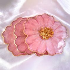 two pink flower shaped plates sitting on top of a white cloth covered tablecloth with gold flecks