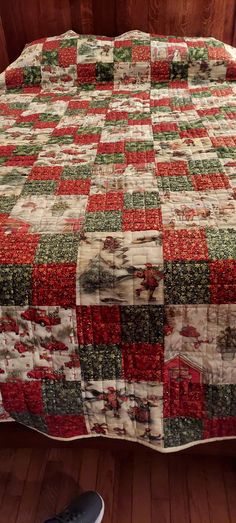 a bed with a red, green and white quilt on it next to a pair of shoes