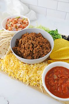 tacos, tortillas and salsa on a cutting board with ingredients in bowls