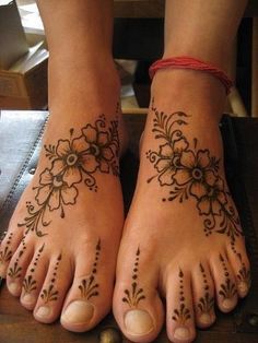 two feet with henna tattoos on them, one has flowers and the other has leaves