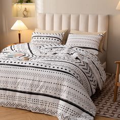 a white bed with black and white bedspread in a bedroom next to a lamp