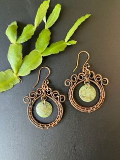 two pairs of earrings sitting on top of a table next to a plant with green leaves