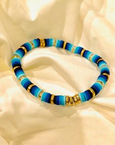 a blue and gold beaded bracelet sitting on top of a white cloth covered bed