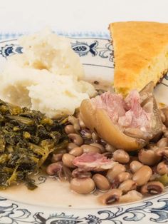 a blue and white plate topped with beans, ham, mashed potatoes and greens