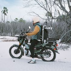 a man riding on the back of a motorcycle through snow covered ground with trees in the background