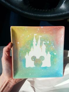 a hand holding up a square coaster with a mickey mouse silhouette painted on the front