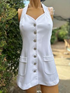 Here is a vintage 1970s white halter polyester tennis dress.Made by Top Seed. Following are the measurements. Bust 32",Waist 28",Hips 38".Made out of a white polyester fabric.Buttons down the front and neck with silver cross buttons. Navy blue top stitching. In nice vintage condition. Please take special consideration of measurements. 1970 sizing was much smaller than today's standards. Take extra special note of length. Tennis dresss were very short not like a regular dress.If you live overseas please email me first before purchasing for mailing cost. Price quoted is for USA only White Lined Halter Neck Mini Dress, White Halter Neck Mini Dress Lined, White Halter Neck Lined Mini Dress, White Retro Mini Dress For Summer, Retro White Mini Dress For Summer, Vintage White Mini Dress For Summer, Vintage White Summer Mini Dress, Vintage White Halter Neck Dress, White A-line Tennis Dress For Summer