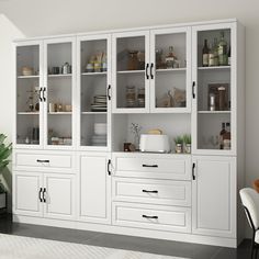 a large white cabinet with glass doors and drawers in the center, next to a dining room table