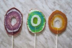 three lollipops with different colors and designs on them sitting on a marble surface