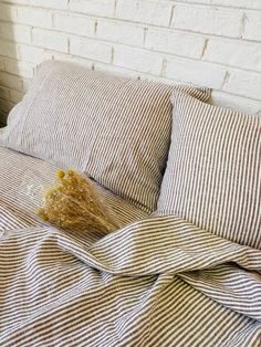 an unmade bed with striped linens and a dried plant on the pillowcase