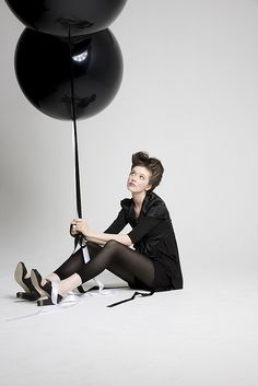 a woman sitting on the ground with some black balloons