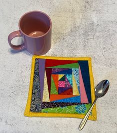 a coffee cup and spoon rest on a table next to a patchwork mug mat