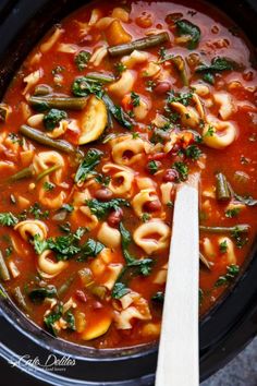 pasta and vegetable soup in a crock pot with a wooden spoon on the side