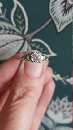 a woman's hand holding an old - fashioned diamond ring in front of a floral wallpaper