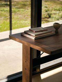 a table with books and a vase on it in front of a glass door that looks out onto a grassy area