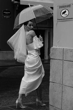 a woman in a wedding dress is holding an umbrella and walking down the street with her hand on her hip