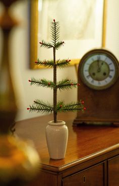 a small christmas tree sitting on top of a wooden table next to a clock in a room