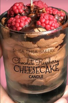 a person holding a chocolate raspberry cheesecake in a glass container with a candle