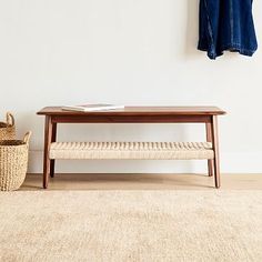 a wooden bench sitting on top of a rug next to a basket and coat rack