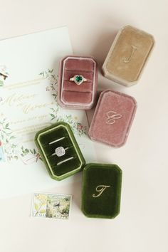 three rings are sitting in velvet boxes next to a wedding card and brochure